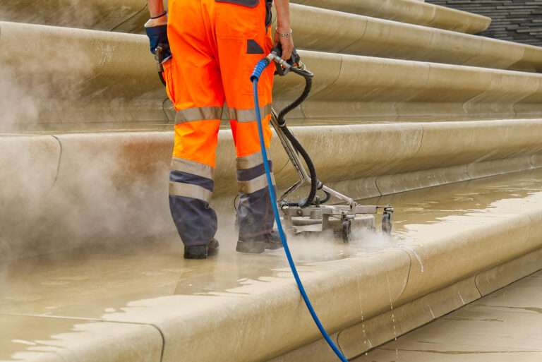 worker washes the pavement. Worker in uniform washes street with street washing machine. Municipal service of city cleaning process. Road worker cleaning city street at morning, disinfection of the street