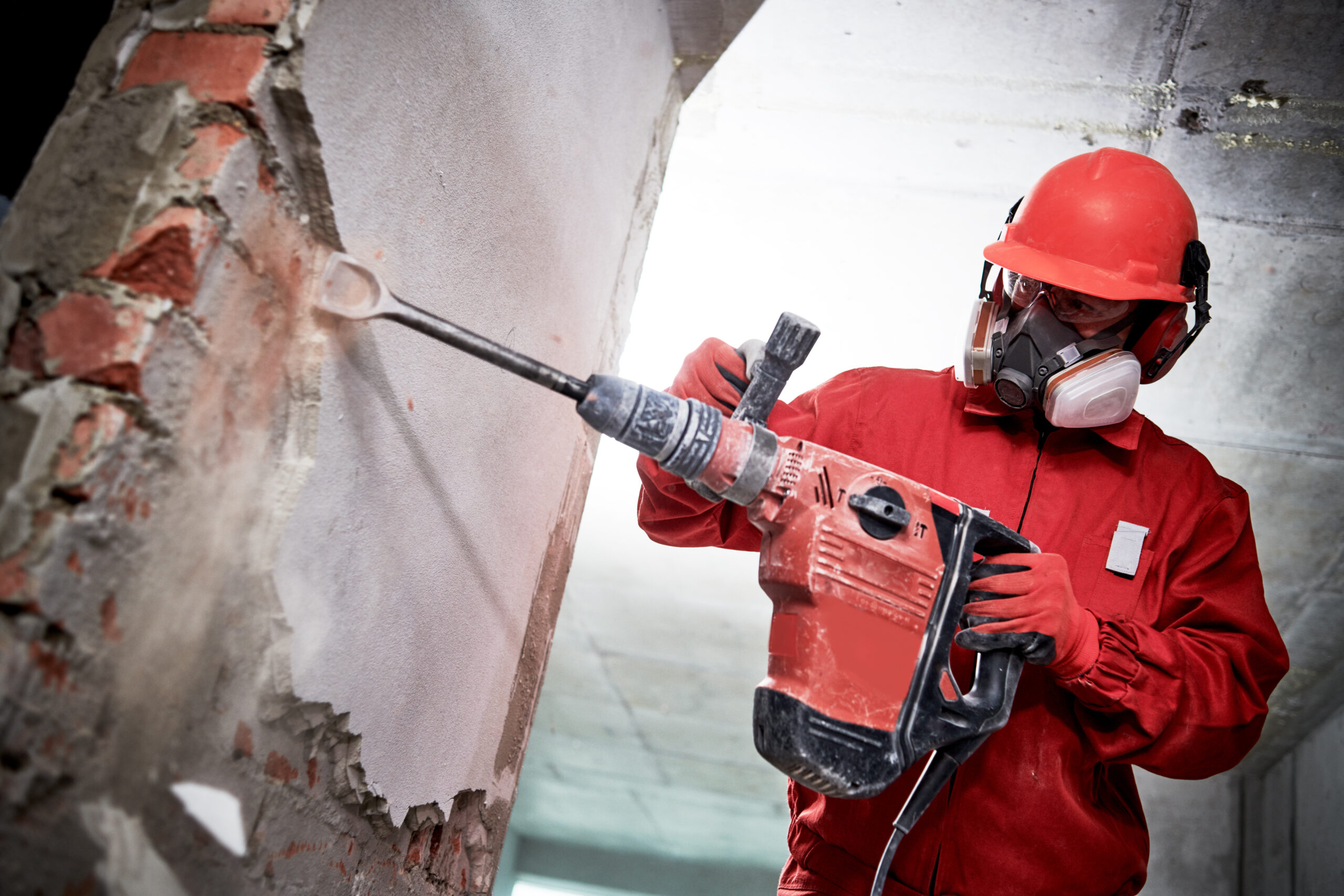 Demolition and destroying. Worker with demolition hammer in personal protection equipment removing interior brick wall plastering